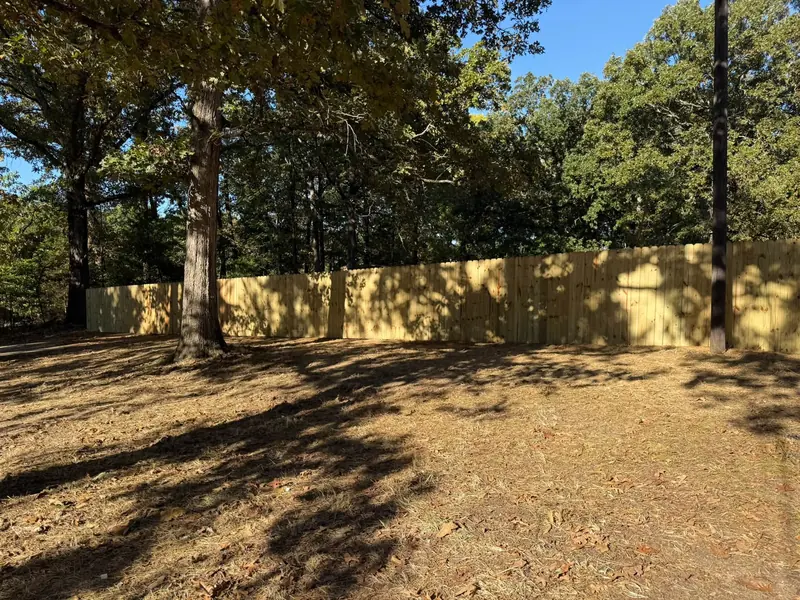 New wood privacy fence across a wooded backyard