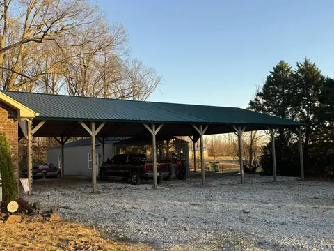 Open-sided pole shelter with a green metal roof over a gravel pad