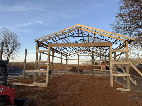 Pole barn frame with wood posts and steel trusses under construction on a cleared site