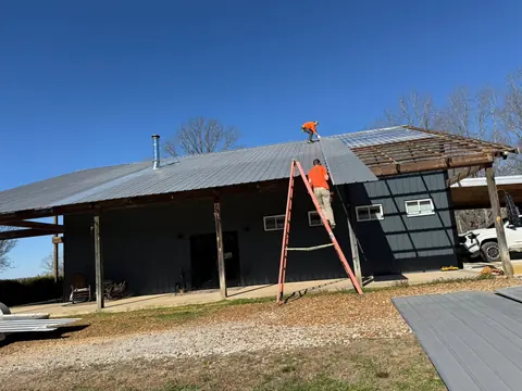 Crew member on a ladder installing metal roofing on a dark-sided building